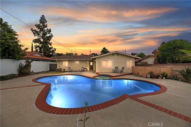 pool at dusk featuring a fenced backyard, a patio area, and a pool with connected hot tub
