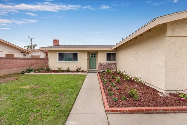 view of exterior entry with stucco siding, a lawn, fence, and a chimney