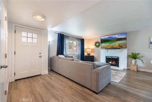 living area featuring baseboards, a brick fireplace, and light wood-style flooring