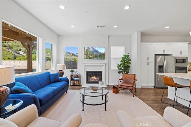 living area with recessed lighting, a glass covered fireplace, dark wood-style floors, and visible vents