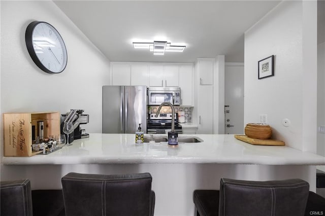 kitchen featuring a peninsula, a breakfast bar area, light countertops, white cabinets, and stainless steel appliances