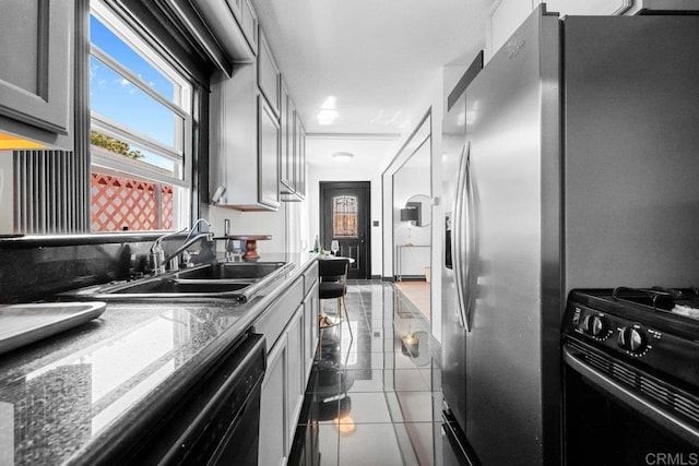 kitchen with tile patterned flooring, a sink, stone counters, and black appliances