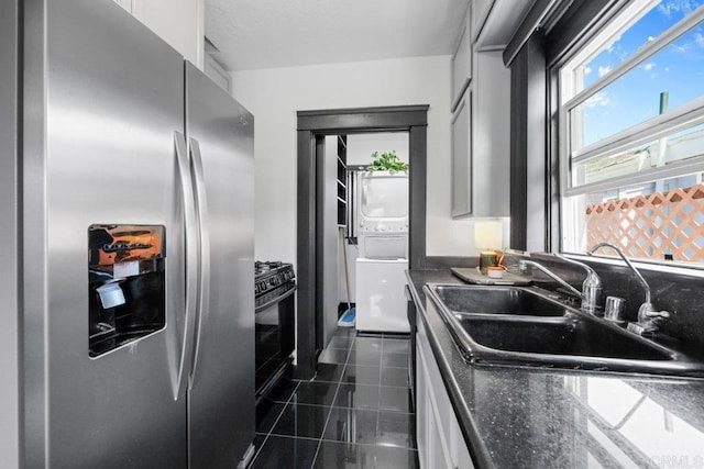 kitchen featuring stacked washer and dryer, a sink, stainless steel fridge with ice dispenser, black range with gas cooktop, and dark tile patterned floors