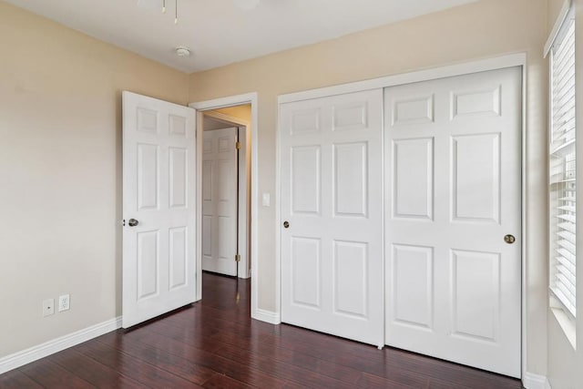 unfurnished bedroom with baseboards, a closet, and dark wood-style flooring