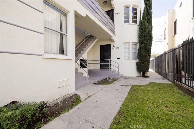 1144 W 57th St, Los Angeles, CA 90037 - doorway to property featuring fence, stucco siding, a yard, and visible vents
