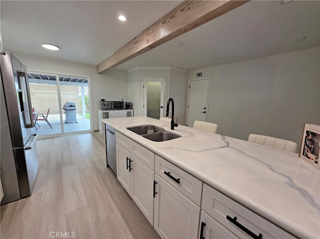 kitchen with a sink, white cabinets, beamed ceiling, appliances with stainless steel finishes, and light stone counters