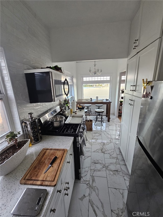 1030 E Ocean Blvd Unit 210, Long Beach, CA 90802 - kitchen with appliances with stainless steel finishes, light marble finish flooring, white cabinetry, a chandelier, and light stone countertops