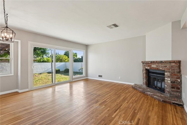 unfurnished living room featuring visible vents, a brick fireplace, wood finished floors, baseboards, and a chandelier