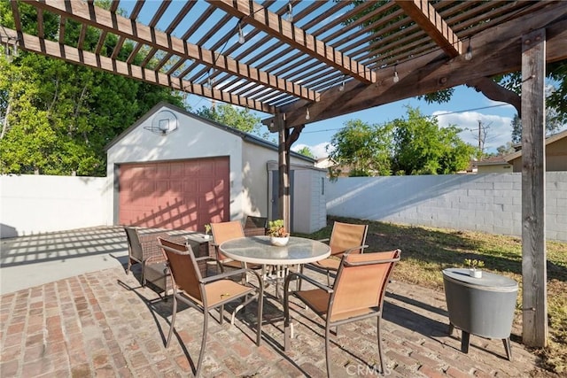 view of patio with a garage, a fenced backyard, an outdoor structure, and outdoor dining space