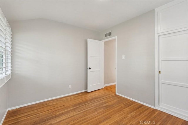 unfurnished bedroom featuring visible vents, vaulted ceiling, baseboards, a closet, and light wood-style floors