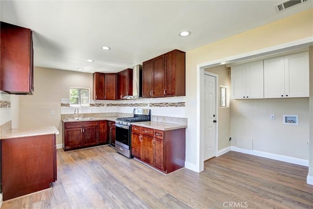 kitchen with a sink, light wood finished floors, stainless steel gas stove, wall chimney exhaust hood, and visible vents