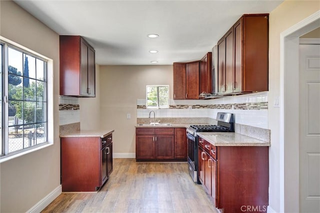 kitchen with backsplash, light wood-type flooring, stainless steel gas stove, a sink, and baseboards