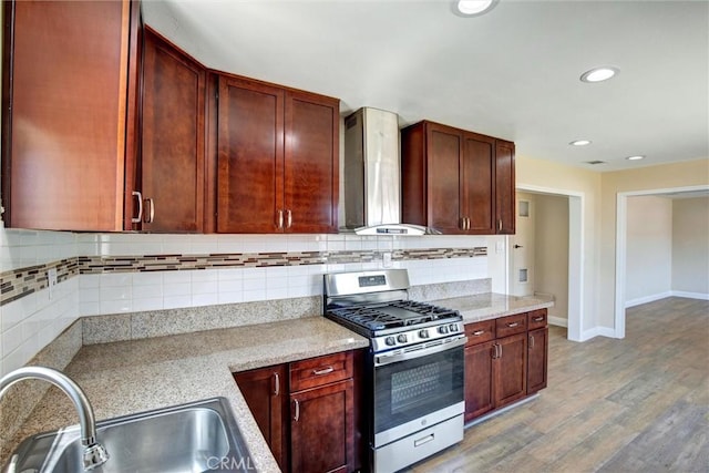 kitchen with wall chimney range hood, backsplash, stainless steel gas stove, a sink, and light wood finished floors
