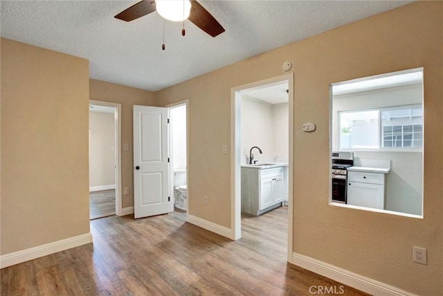 interior space featuring ceiling fan, a textured ceiling, wood finished floors, a sink, and baseboards