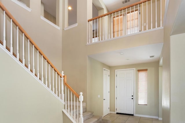 tiled entryway with visible vents, baseboards, stairs, and a high ceiling