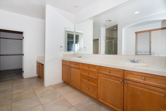 full bath with double vanity, a sink, a walk in closet, and a shower stall