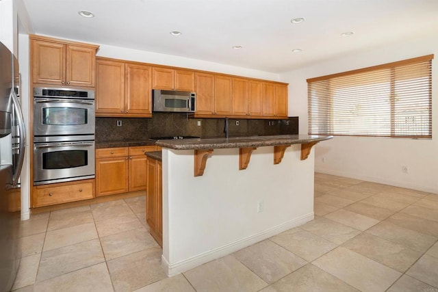 kitchen featuring light tile patterned flooring, a kitchen breakfast bar, dark stone counters, tasteful backsplash, and appliances with stainless steel finishes