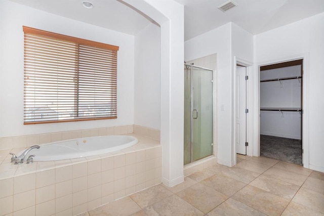 full bath featuring a walk in closet, baseboards, visible vents, a garden tub, and a stall shower