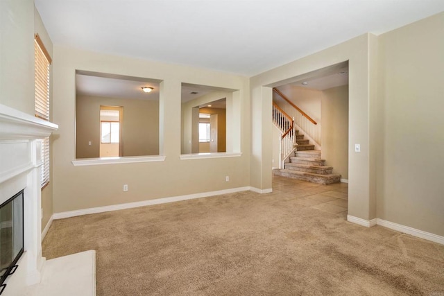 unfurnished living room with a fireplace with flush hearth, baseboards, carpet, and stairs