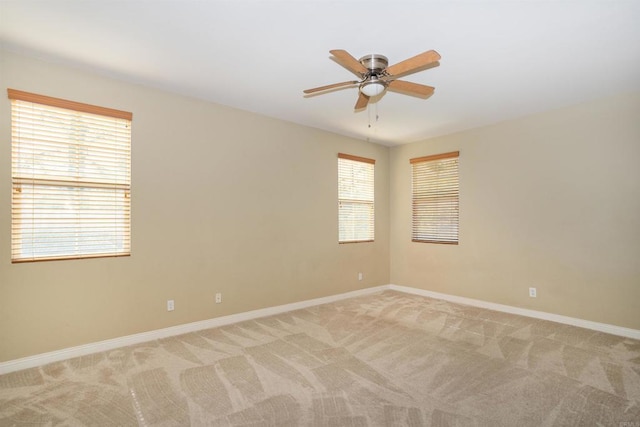 unfurnished room with light colored carpet, baseboards, ceiling fan, and a wealth of natural light