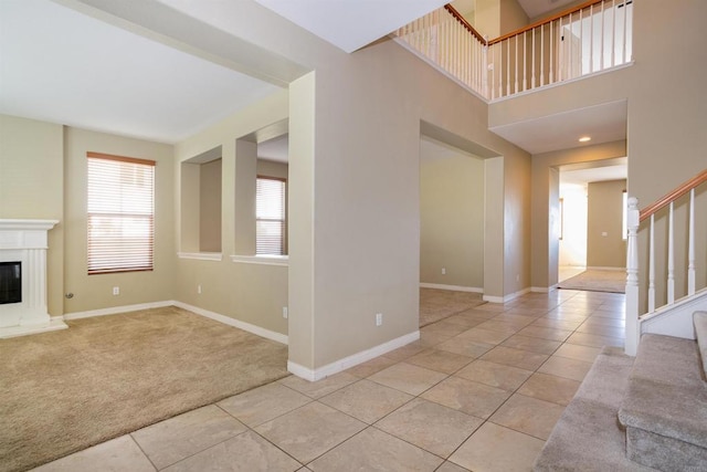 carpeted entrance foyer featuring stairs, baseboards, a glass covered fireplace, and tile patterned flooring