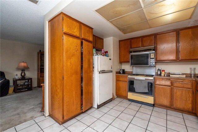 kitchen with freestanding refrigerator, stainless steel range with gas stovetop, brown cabinets, and light tile patterned floors