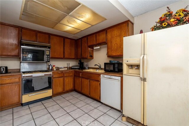 kitchen with white appliances, a sink, brown cabinetry, and light tile patterned floors