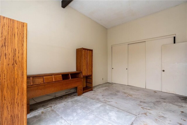 unfurnished bedroom with unfinished concrete floors, a closet, high vaulted ceiling, and beamed ceiling