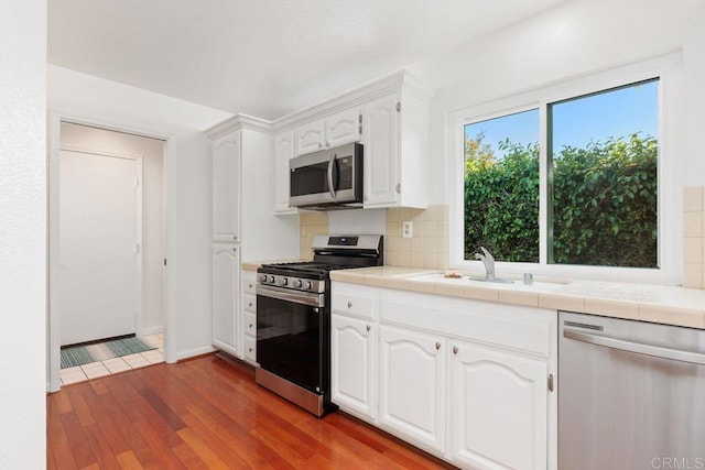 814 Okra Ct, Carlsbad, CA 92011 - kitchen with stainless steel appliances, tile counters, white cabinets, decorative backsplash, and wood finished floors