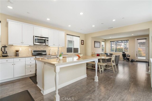 2677 E Tyler St, Long Beach, CA 90810 - kitchen with appliances with stainless steel finishes, decorative backsplash, a kitchen island with sink, and dark wood-style floors