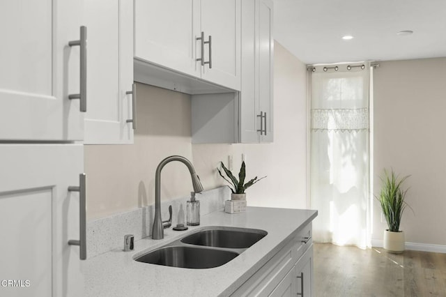 kitchen featuring wood finished floors, a sink, light stone counters, white cabinets, and recessed lighting
