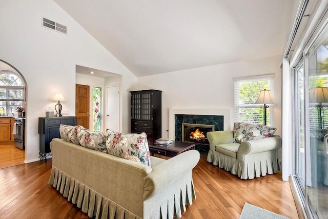 living room featuring visible vents, a high end fireplace, wood finished floors, and a healthy amount of sunlight