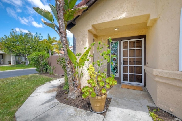 property entrance with a lawn, stucco siding, and fence