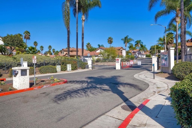 view of street featuring a residential view, sidewalks, curbs, a gate, and street lights