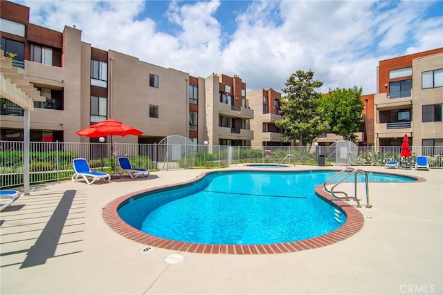 community pool with a patio, a hot tub, and fence