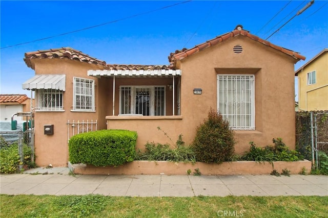mediterranean / spanish home with fence, stucco siding, and a tile roof