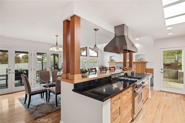 kitchen featuring stainless steel stove, island exhaust hood, french doors, light wood-style flooring, and hanging light fixtures
