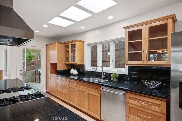 kitchen featuring appliances with stainless steel finishes, ventilation hood, a sink, a skylight, and dark stone countertops