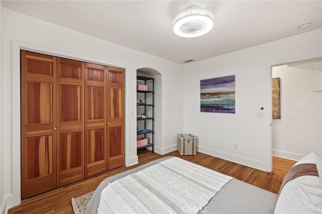 bedroom featuring radiator heating unit, arched walkways, baseboards, and wood finished floors