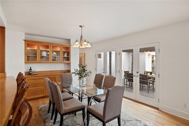 dining space with french doors, light wood-style floors, a chandelier, and baseboards