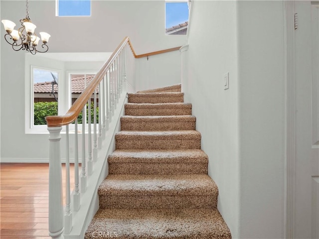 stairway featuring an inviting chandelier and wood finished floors