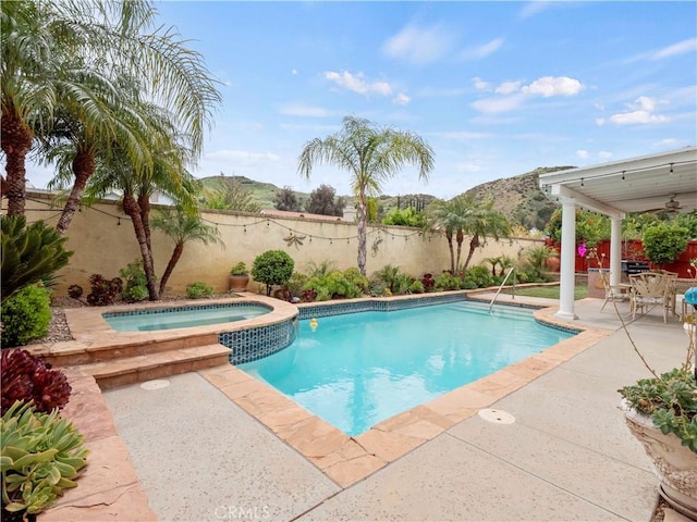 view of swimming pool with a fenced backyard, a mountain view, a pool with connected hot tub, and a patio area