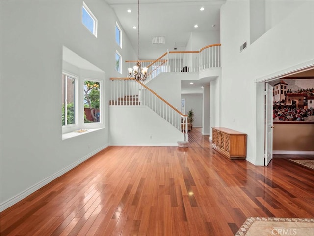 unfurnished living room with visible vents, a high ceiling, stairway, hardwood / wood-style flooring, and a wealth of natural light