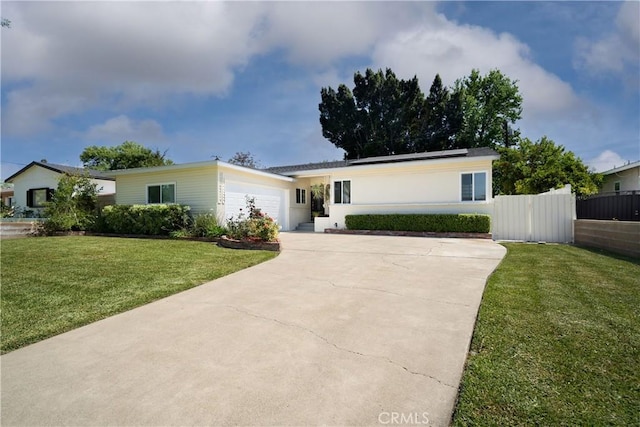 ranch-style house featuring fence, a garage, a front yard, roof mounted solar panels, and concrete driveway
