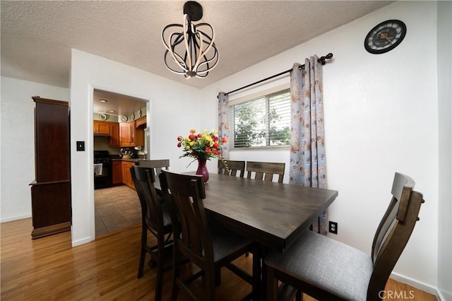 dining space with baseboards, a textured ceiling, a notable chandelier, and light wood-style flooring
