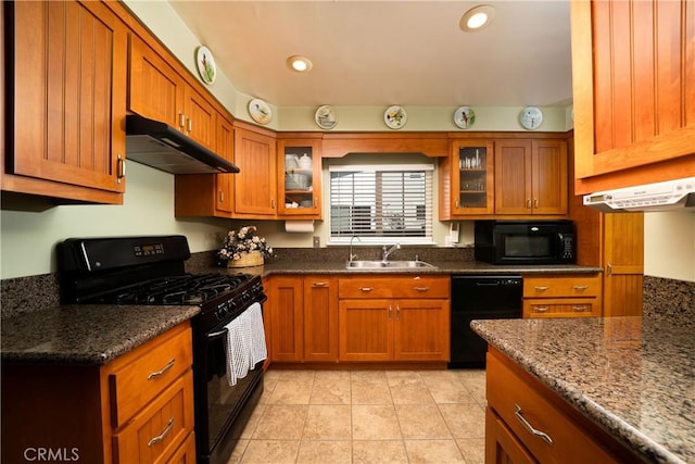 kitchen featuring brown cabinetry, a sink, black appliances, glass insert cabinets, and under cabinet range hood