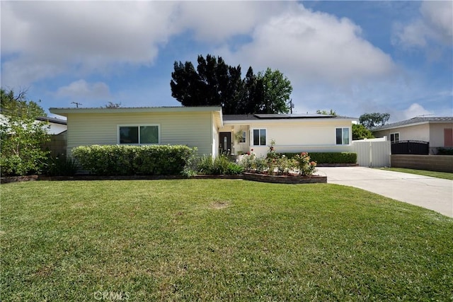 ranch-style house featuring concrete driveway, fence, solar panels, and a front yard