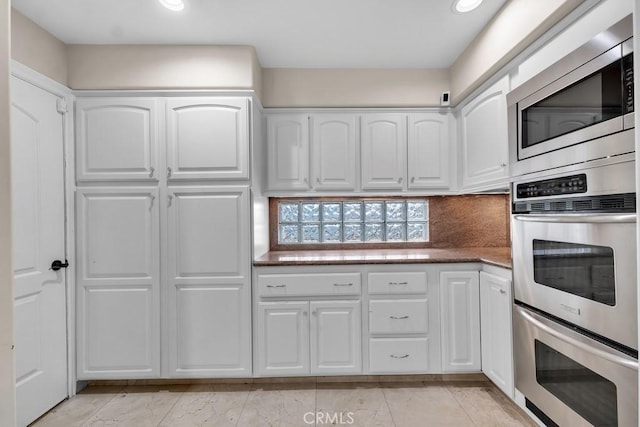kitchen featuring appliances with stainless steel finishes, white cabinets, decorative backsplash, and dark stone countertops
