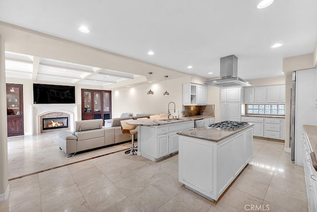 kitchen with a peninsula, white cabinetry, island exhaust hood, a sink, and stainless steel gas stovetop