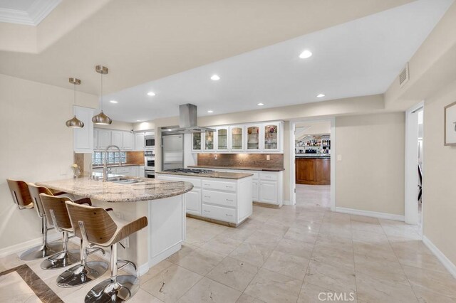 kitchen with visible vents, island range hood, tasteful backsplash, a sink, and a peninsula